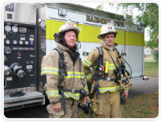 Two firefighters standing in front of a fire truck, ready for action.